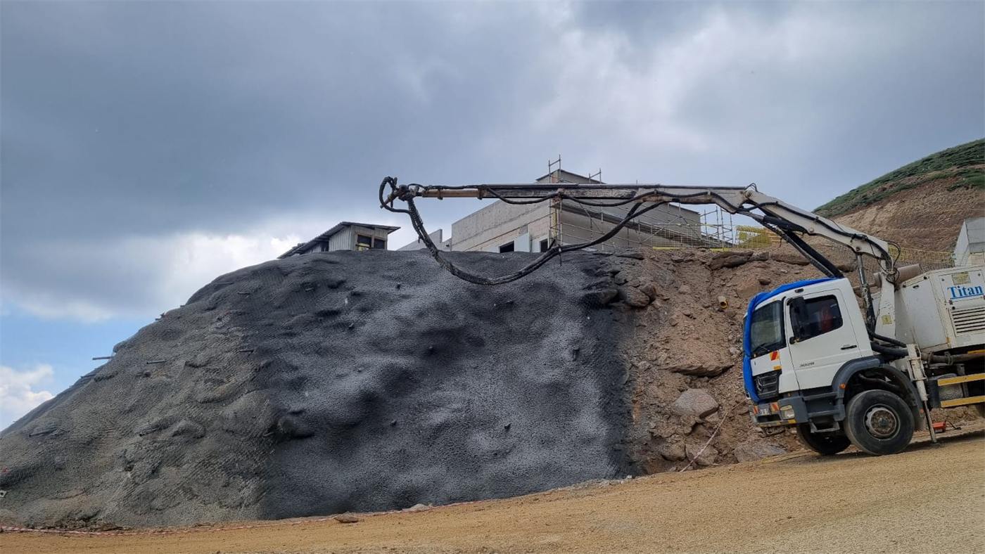 Slope half covered with fresh shotcrete, spray truck below