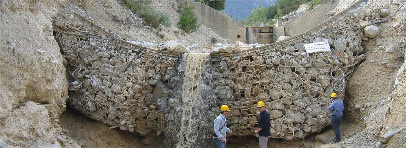 Gabion check dam with water overflowing, engineers inspecting